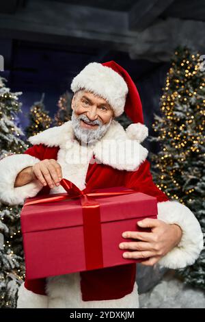 Le Père Noël partage le bonheur avec un cadeau rouge vif dans un cadre serein de forêt hivernale. Banque D'Images