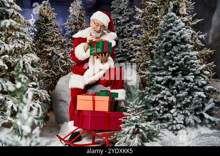 Le Père Noël est heureux d'organiser des cadeaux colorés dans un cadre de forêt enneigée rempli d'arbres. Banque D'Images