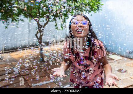 Goiania, Goias, Brésil – 13 octobre 2024 : une fille s’amuse dans son jardin et des bulles de savon autour. Banque D'Images