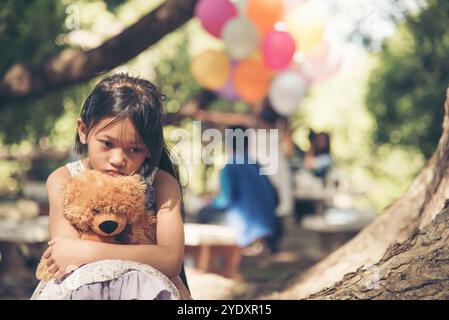 Fille triste embrassant ours en peluche tristesse seul dans le parc de jardin vert. Fille solitaire se sentant triste malheureux assis à l'extérieur avec le jouet meilleur ami. Autisme enfant pl Banque D'Images