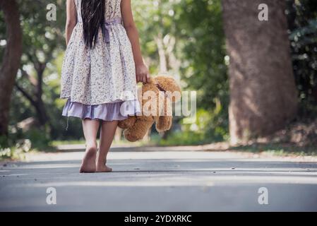 Triste fille embrassant le ours en peluche tristesse seule dans le parc de jardin vert. Solitaire fille se sentant triste malheureux marche à l'extérieur avec le meilleur jouet ami. Autisme enfant pl Banque D'Images