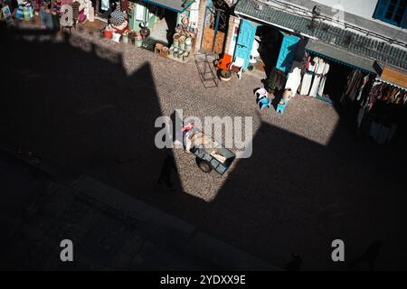 Une vue à vol d'oiseau d'un commerçant de rue marocain poussant une charrette en bois dans les rues pavées de la médina d'Essaouira. Banque D'Images