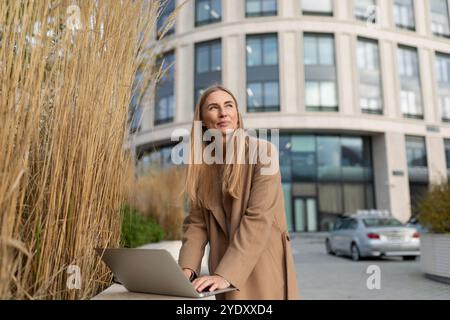 Une femme d'affaires utilise son ordinateur portable à l'extérieur d'un immeuble de bureaux moderne Banque D'Images