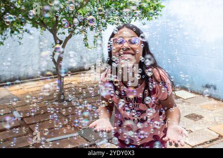 Goiania, Goias, Brésil – 13 octobre 2024 : une fille s’amuse dans son jardin et des bulles de savon autour. Banque D'Images