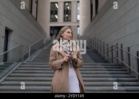 Une femme d'affaires se tient sur les marches à l'extérieur d'un centre d'affaires, levant les yeux Banque D'Images