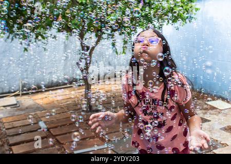 Goiania, Goias, Brésil – 13 octobre 2024 : une fille s’amuse dans son jardin et des bulles de savon autour. Banque D'Images