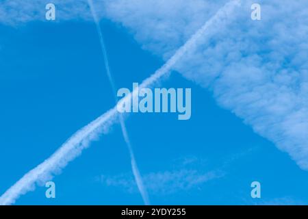 Traînées de vapeur dans le ciel bleu provenant des avions qui traversent et s'étendent plus larges que les traces étroites d'origine se fanent en motifs à bords plumes Banque D'Images