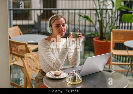 Une jeune femme appréciant un délicieux café tout en travaillant sur un ordinateur portable dans un cadre de café Banque D'Images