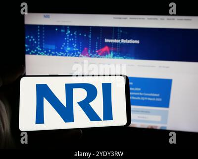 Personne tenant un smartphone avec le logo de la société Nomura Research Institute Ltd. (NRI) sur l'écran en face du site Web. Concentrez-vous sur l'affichage du téléphone. Banque D'Images