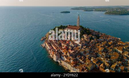 Nichée le long des eaux Azur, Rovinj captive avec ses bâtiments pittoresques et ses toits vibrants, tandis que le soleil se couche, projetant une lueur chaude sur le paysage serein et invitant à l'exploration. Banque D'Images