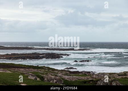 Un rivage rocheux rencontre les vagues agitées de l'océan Atlantique sous un ciel nuageux, capturant la côte sauvage et accidentée de l'Irlande Banque D'Images