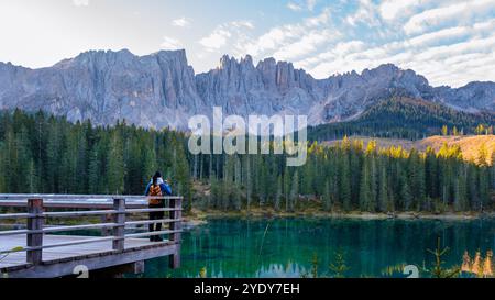 Un voyageur solitaire se tient sur un pont en bois, contemplant les eaux turquoises sereines reflétant les majestueuses Dolomites. Lac Carezza ou Karersee Dolomites en Italie. Banque D'Images