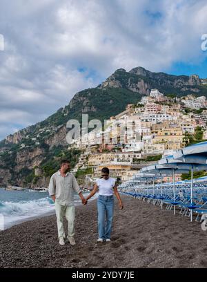 Un couple profite d'une promenade sereine le long de la côte de galets de la côte amalfitaine, entouré de charmants villages à flanc de falaise et d'un ciel sombre, capturant l'essence romantique de la beauté côtière de l'Italie. Banque D'Images