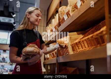 Une jeune femme stocke du pain fraîchement cuit dans une boulangerie confortable avec une atmosphère vraiment accueillante Banque D'Images