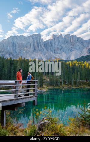 Deux randonneurs se tiennent sur une jetée en bois, trempant dans la vue imprenable sur les Dolomites et le vibrant lac émeraude ci-dessous, le lac Carezza ou Karersee Dolomites en Italie. Banque D'Images