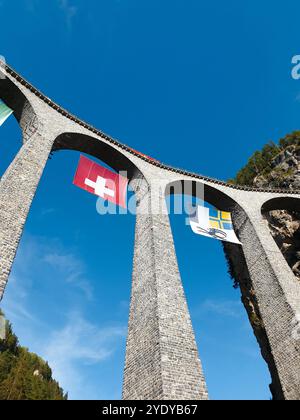 En regardant Landwasserviadukt. Viaduc ferroviaire courbe dans les alpes d'Abula. Le train rouge passe le pont ferroviaire et entre dans un tunnel dans la falaise. Banque D'Images