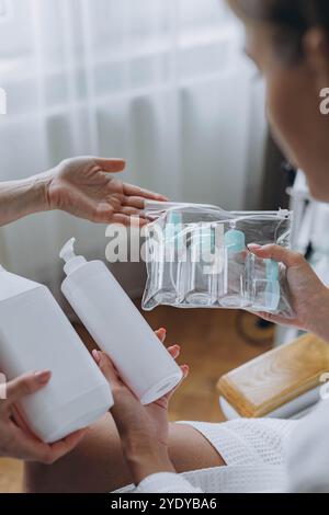 Cosmétologue montre au client un produit cosmétique et des bouteilles en plastique de voyage, maquette de bouteille de crème. Photo de haute qualité Banque D'Images