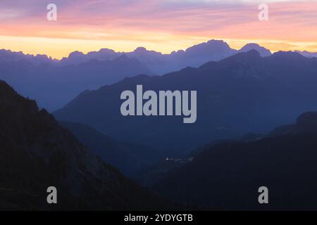 Vue crépusculaire sur les Dolomites italiennes depuis le col de Giau, avec un coucher de soleil coloré illuminant les montagnes escarpées et un village lointain Selva di CAD Banque D'Images