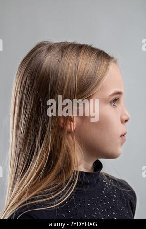 Portrait studio d'une jeune fille aux longs cheveux blonds, portant une chemise à col roulé sombre, présentant une expression neutre alors qu'elle regarde au loin Banque D'Images