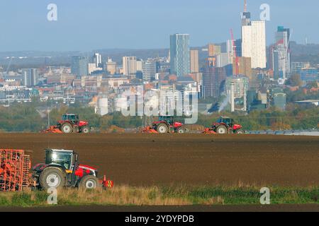 Agriculteurs labourant les champs avec le centre-ville de Leeds comme toile de fond Banque D'Images