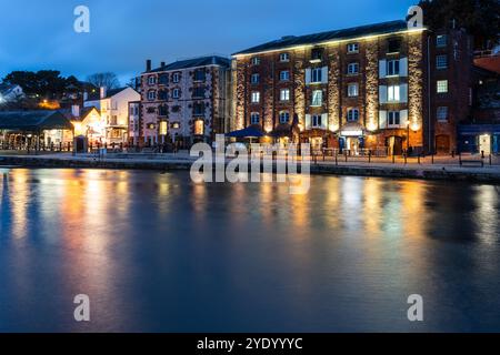 Les entrepôts convertis sont éclairés la nuit au quai régénéré d'Exeter, sur les rives du River exe. Banque D'Images