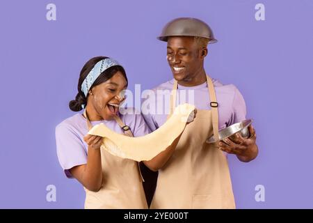 Des temps de cuisson romantiques. Jeune couple noir avec pâte à cuire sur fond lilas Banque D'Images