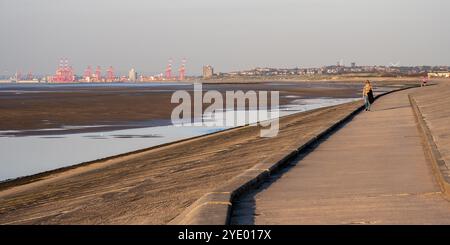 Les gens marchent le long du front de mer à Leasowe Beach sur le Wirral, avec Liverpool Docks au loin. Banque D'Images