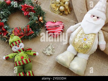 Père Noël portant une tenue blanche et dorée pour la célébration des vacances de Noël le 25 décembre avec bonhomme de neige, guirlande et boules de Noël. Banque D'Images