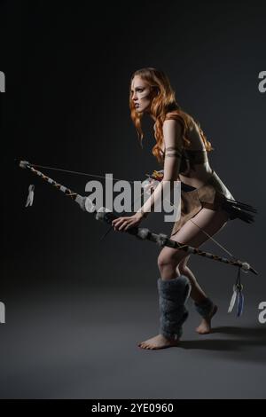 Femme habillée en tenue de survie pose avec un arc dans un cadre de studio Banque D'Images