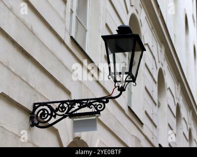 Lampadaire classique en fer noir sur la façade du bâtiment historique, avec des ferronneries ornées et des lignes architecturales épurées contre un mur extérieur neutre Banque D'Images