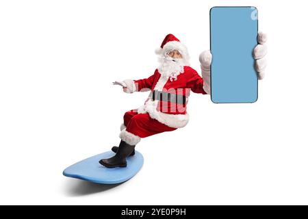 Père noël chevauchant une planche de surf et tenant un téléphone portable isolé sur fond blanc Banque D'Images