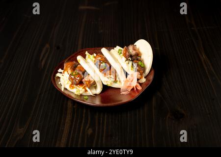 Petits pains bao avec poitrine de porc BBQ et coleslaw sur une assiette brune. Côté de gingembre mariné Banque D'Images