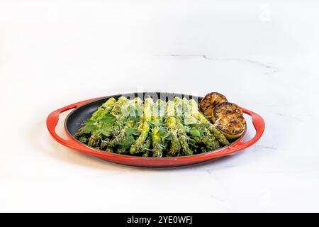 Un plat de service rond avec asperges grillées, citrons grillés et persil italien haché. Banque D'Images