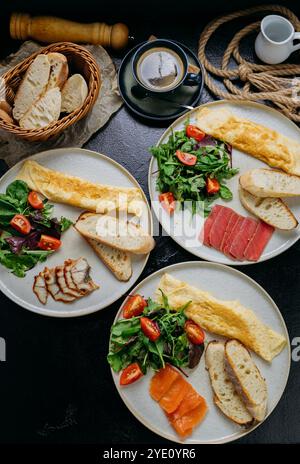 Assiettes petit déjeuner avec omelettes, légumes-feuilles, pain, saumon fumé, thon poêlé, et des tranches de poulet Banque D'Images