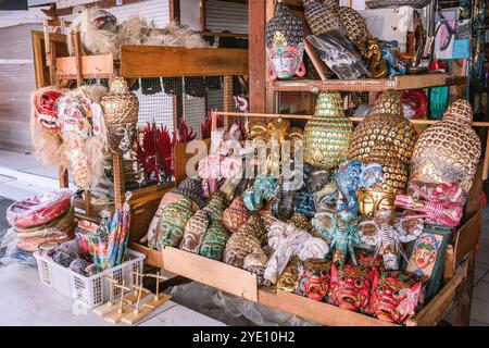 Masques et statues balinais traditionnels colorés représentant des démons, des têtes de bouddha et des éléphants sont exposés sur les étagères en bois d'un stand de souvenirs dans un Banque D'Images