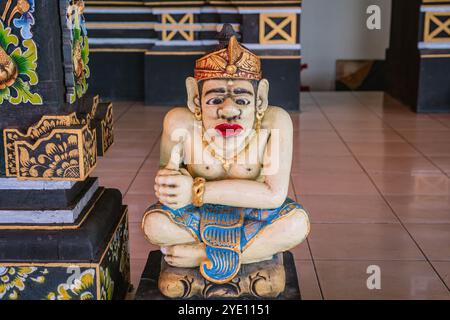 Statue en bois représentant une divinité assise vêtue de vêtements et de bijoux traditionnels, gardant l'entrée du temple Tanah Lot à Bali Banque D'Images