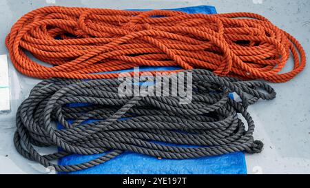 Deux longueurs de corde, Une corde rouge enroulée à côté d'une corde noire sur une bâche bleue sur un pont de bateau. Banque D'Images