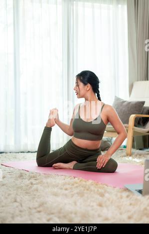 Une femme asiatique attrayante et saine en vêtements de sport pratique le yoga à la maison, étirant son corps sur un tapis de yoga. bien-être et mode de vie sain concepp Banque D'Images