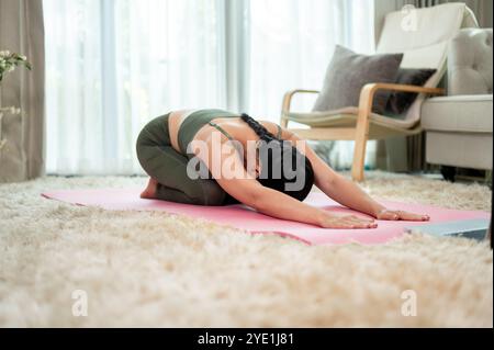 Une femme asiatique attrayante et saine en vêtements de sport pratique le yoga à la maison, étirant son corps sur un tapis de yoga. bien-être et mode de vie sain concepp Banque D'Images