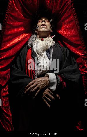 Acteur habillé comme Dracula couché sur un cercueil de velours rouge Banque D'Images