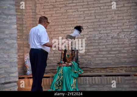 Kihva, Ouzbékistan ; septembre, 21,2024:une femme vêtue de la tenue nationale traditionnelle ouzbèke est assise, engagée dans la conversation avec un homme. Banque D'Images