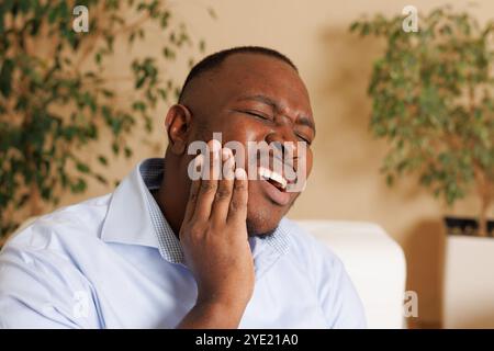 bel homme afro-américain tenant sa joue de mal de dents à la maison, soins dentaires d'urgence, dentalgie Banque D'Images