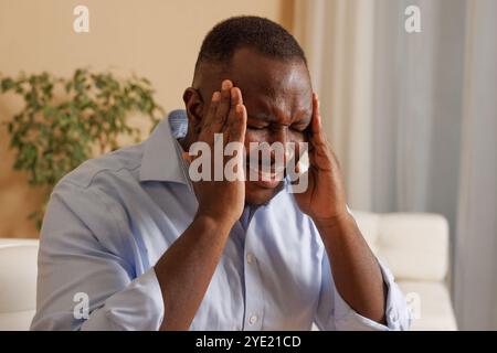 Gros plan d'un homme afro-américain épuisé éprouvant des maux de tête, migraine, surmenage de travailler à l'ordinateur, un gars triste est malade, a besoin d'un traitement Banque D'Images