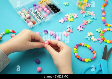 Petite fille a fait des bracelets sur fond bleu. Bijoux en perles faits à la main pour enfants. Colliers et bracelets fabriqués à partir de perles et perles multicolores. Bricolage Banque D'Images