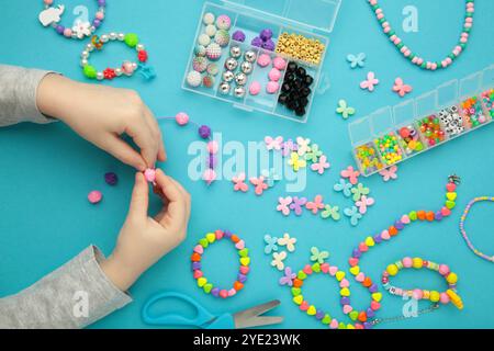 Petite fille a fait des bracelets sur fond bleu. Bijoux en perles faits à la main pour enfants. Colliers et bracelets fabriqués à partir de perles et perles multicolores. Bricolage Banque D'Images