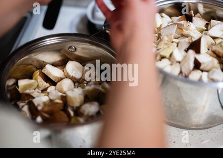 Une vue rapprochée des mains manipulant des champignons frais dans des pots en acier inoxydable, prêts pour la cuisson. L'image capture l'essence de la cuisine maison et de l'orgue Banque D'Images