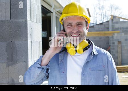 travailleur de la construction au téléphone avec écouteurs antibruit Banque D'Images