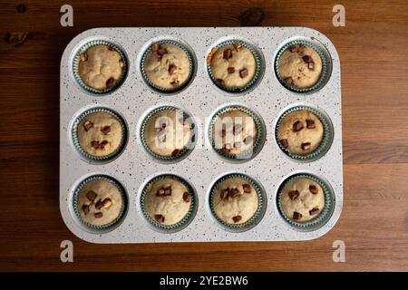 Vue de dessus de muffins faits maison avec des pépites de chocolat, fraîchement cuits dans une plaque de cuisson mouchetée, surface en bois, fond naturel Banque D'Images