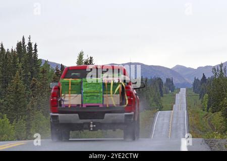 Un camion rouge avec des marchandises volumineuses monte et descend une route droite bordée de forêts et de montagnes, Richardson Highway, Alaska, États-Unis, Amérique du Nord Banque D'Images