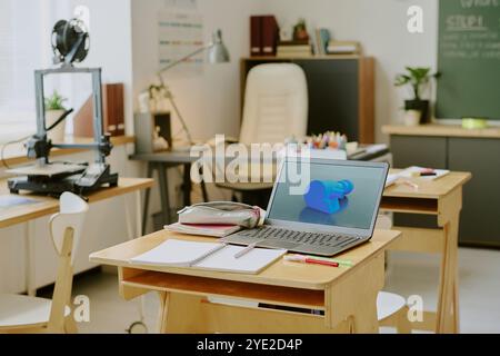 Salle de classe bien agencée avec ordinateur portable ouvert et cahiers éparpillés et stylos sur le bureau entouré de chaises et d'outils éducatifs dans la lumière du jour douce Banque D'Images